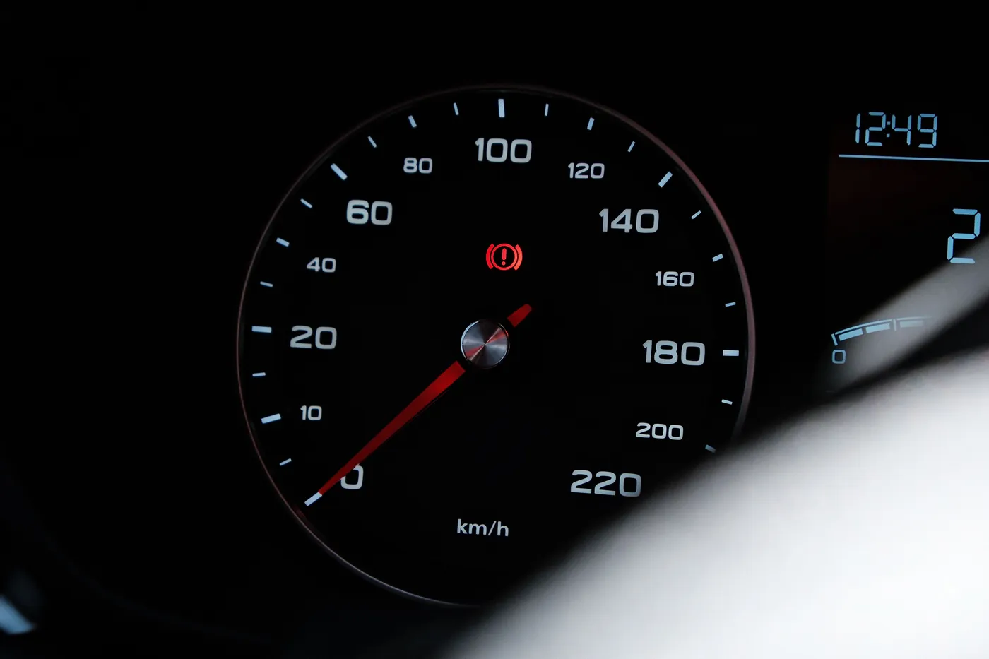 A speedometer at zero with the red brake warning lamp lit