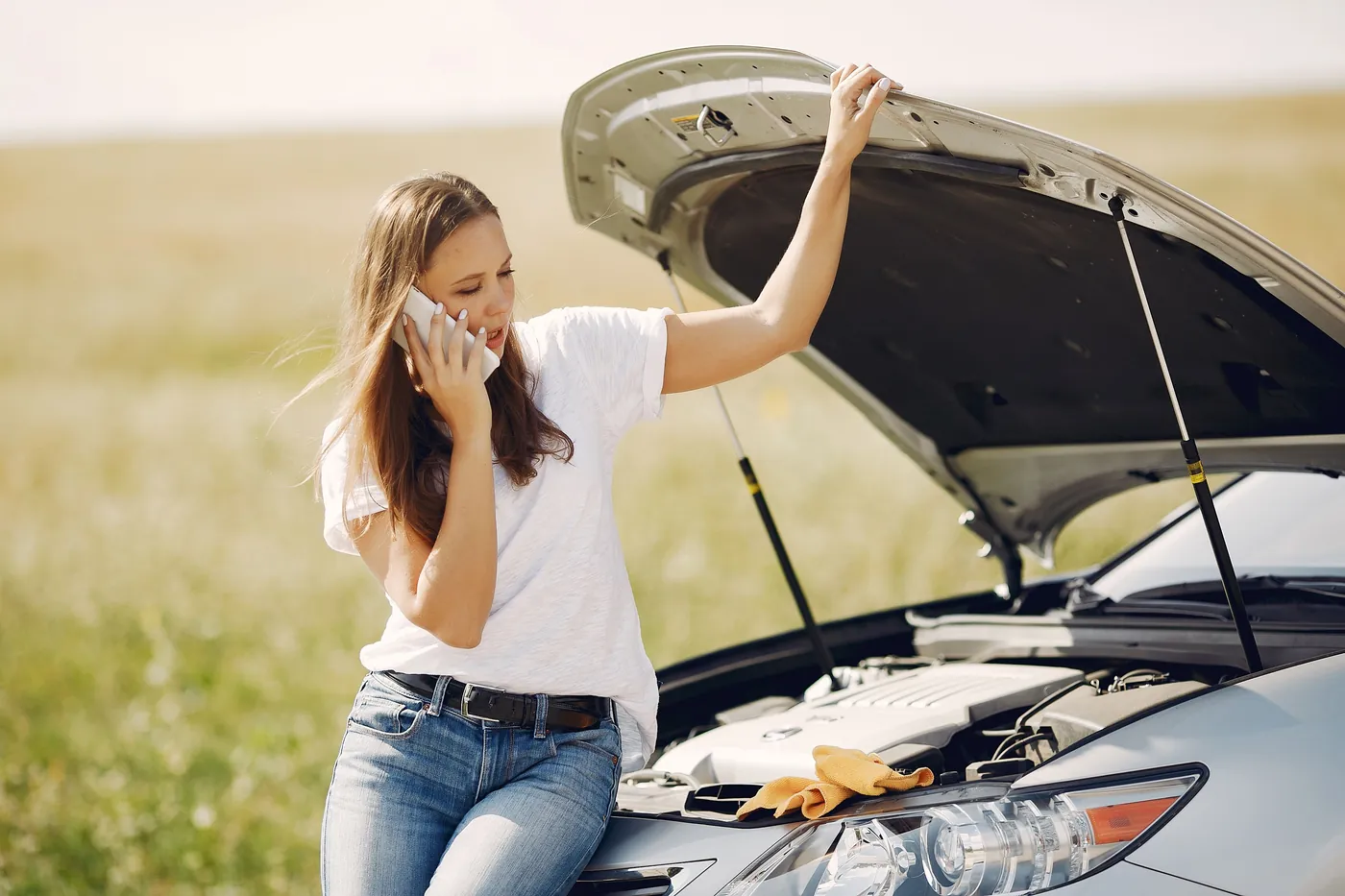 A driver on the phone beside her car with the hood up