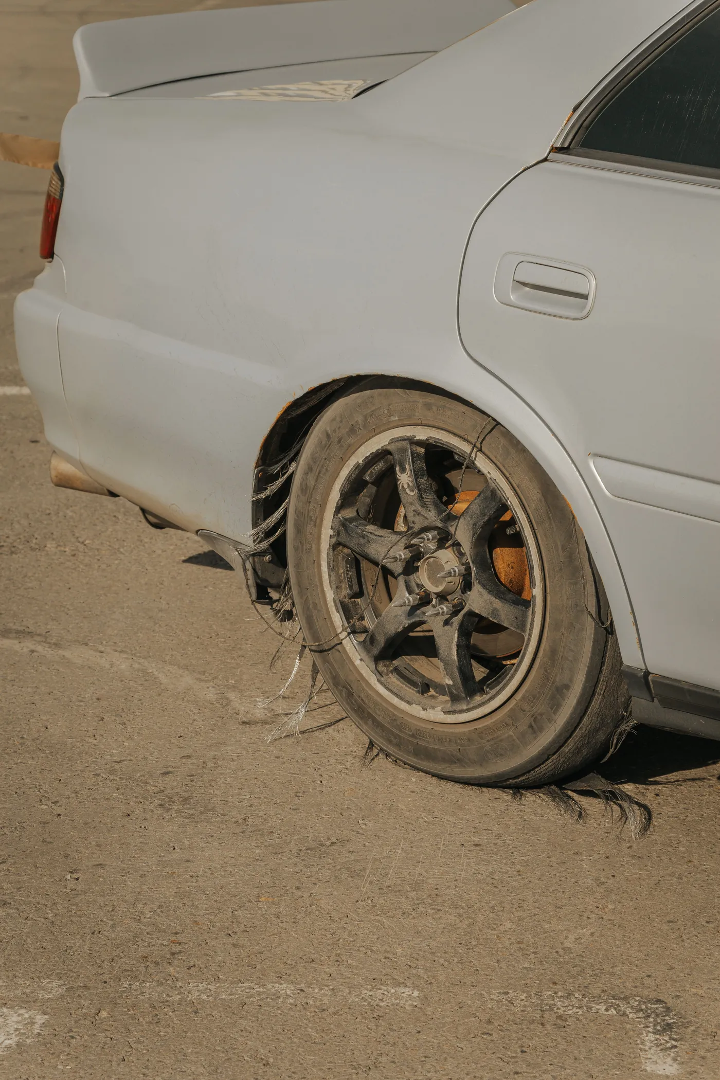 A white car with a flat rear tyre on gravel