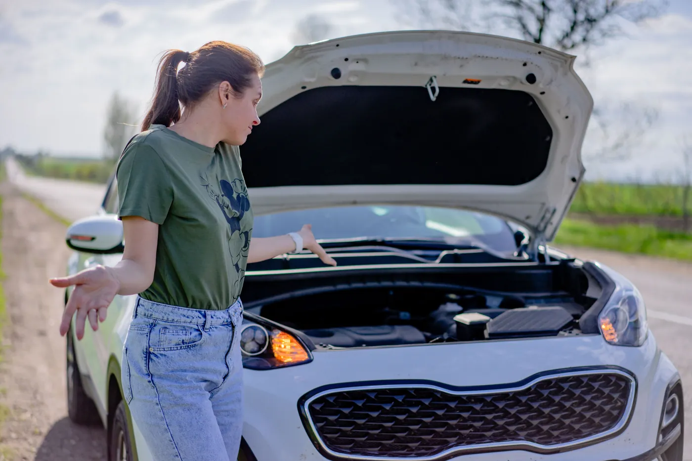 A driver looking into her car's open engine bay with the hazard lights on