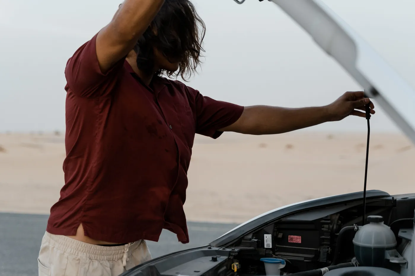A driver wiping his brow over an open engine bay on an empty road