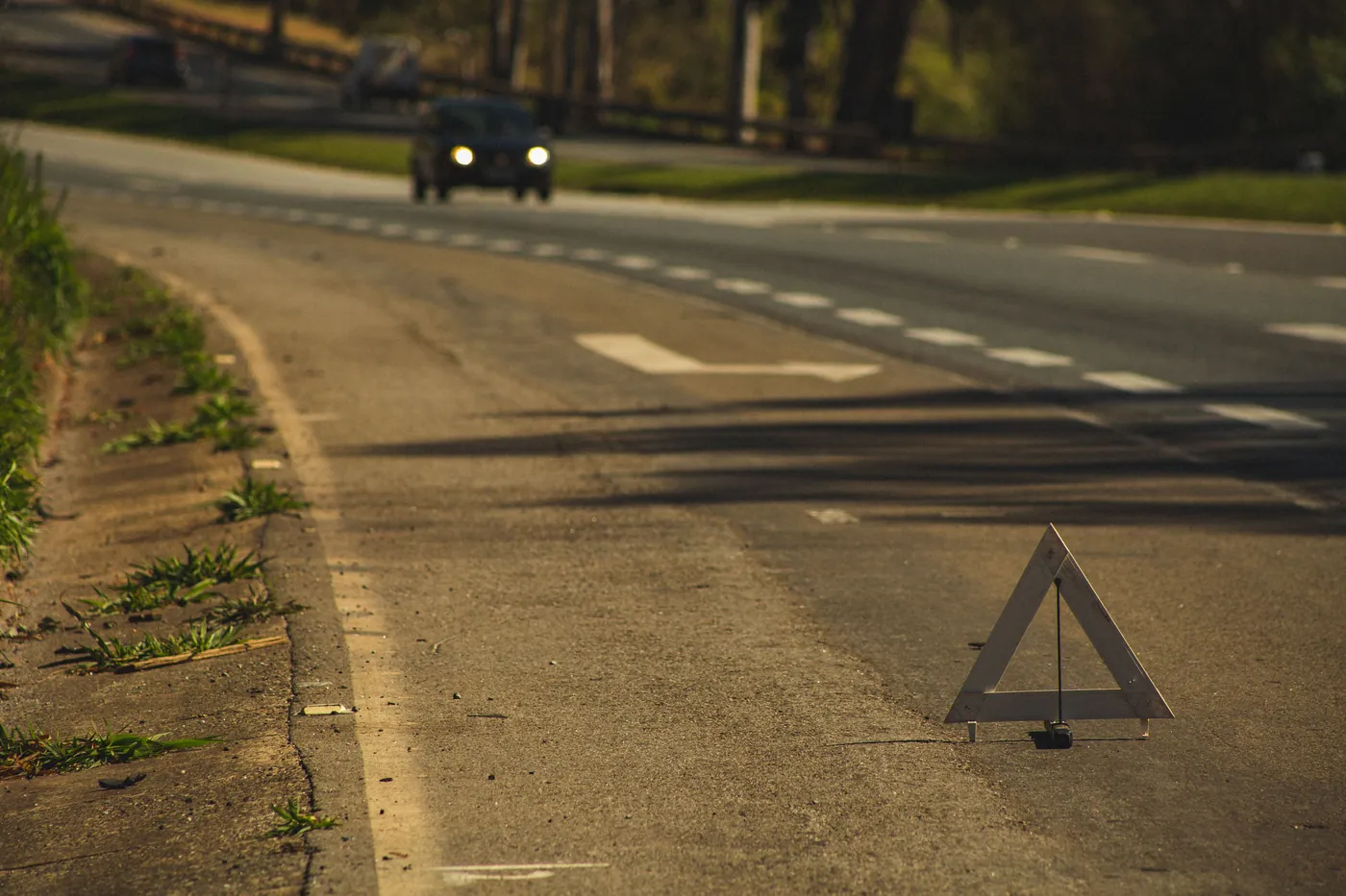 A reflective warning triangle on the road at dusk with a car's headlights approaching