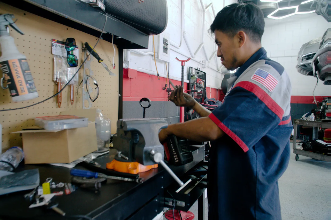 A technician at the workbench with tools on the pegboard behind