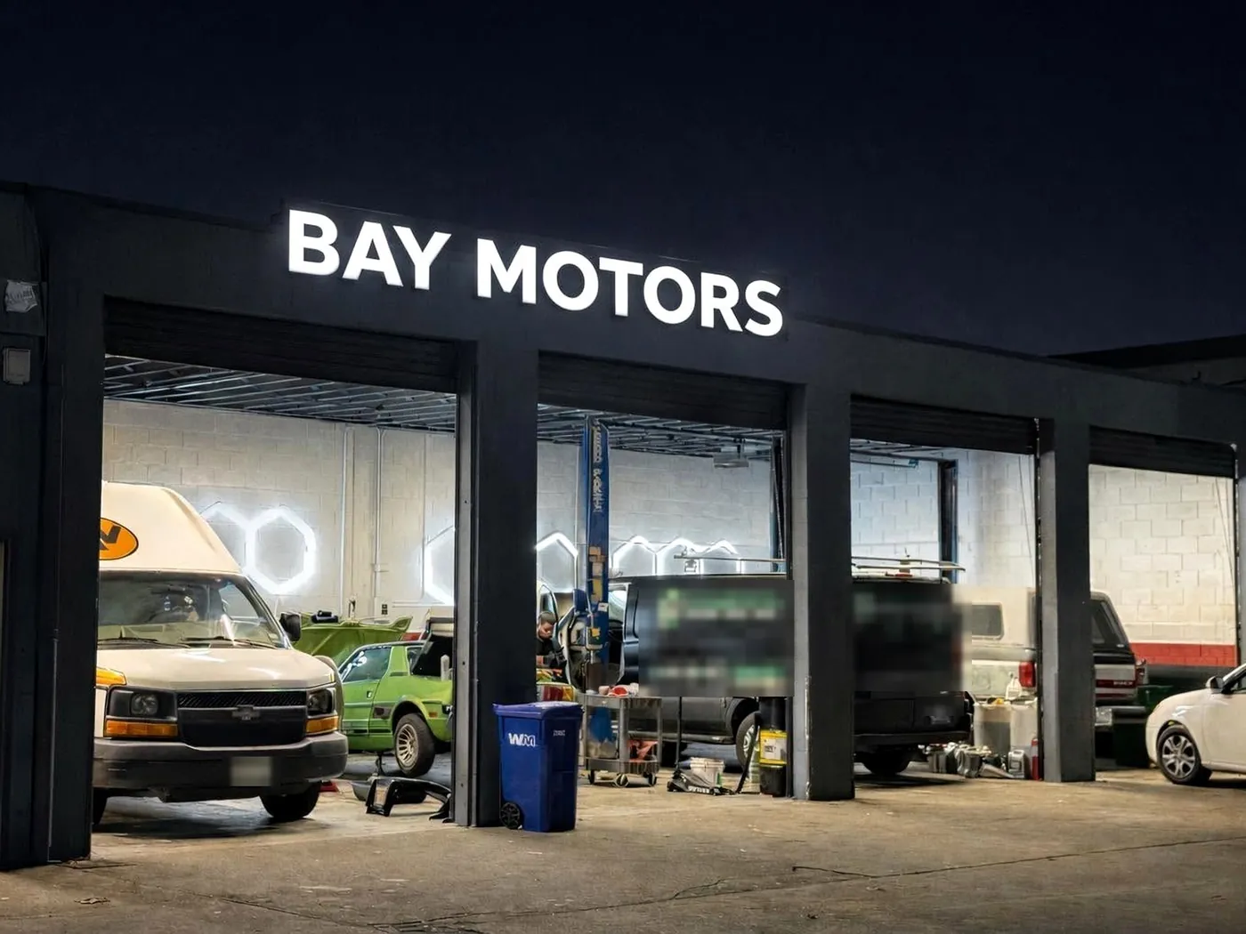 Bay Motors shop front at dusk with the lit sign and open bays