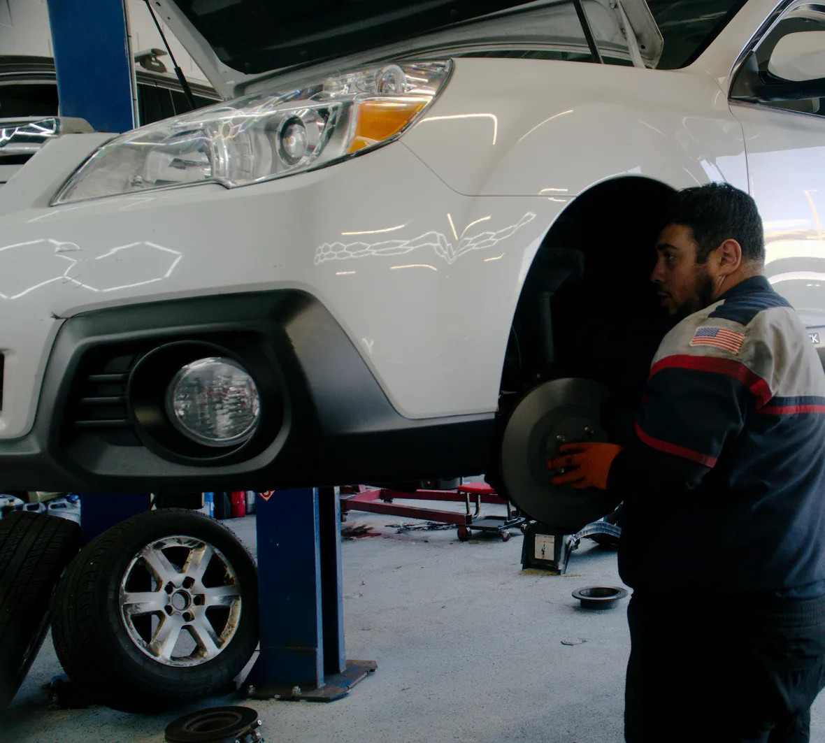A white SUV on the lift with a technician at the front wheel